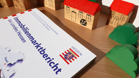 Immobilienmarktbericht auf Tisch liegend mit Holzspielhäusern