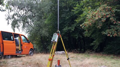 Messstation Satellitenvermessung Orangefarbener Messbus, aufgebaute Satellitenantenne, auf einer Waldlichtung