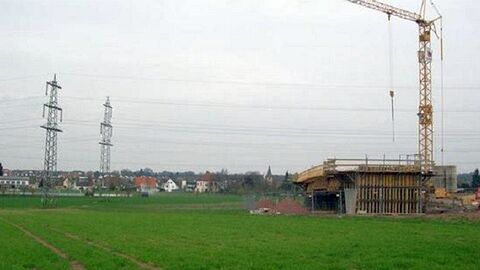 Im Bau befindliche Brücke auf einem Feld, rechts daneben ein Baukran, im Hintergrund Strommasten