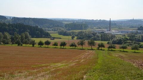 Blick über Felder auf eine Fabrik, links Wälder