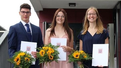 Drei Absolventen mit Zeugnisse und Blumen auf einer Treppe