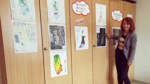 Frau Marianne Kaiser vor einer Wand mit Luftbildern, Kartenausschnitten und weiteren Zetteln