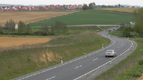 Straße mit einem Auto zwischen Feldern, am Horizont Häuser