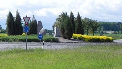 Verkehrskreisel mit Skulptur und Straßenschildern, im Hintergrund Bäume