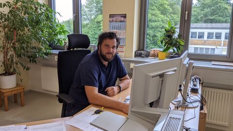 Herr Marc Trennheuser an einem Schreibtisch mit zwei Monitoren, Blick zur Kamera