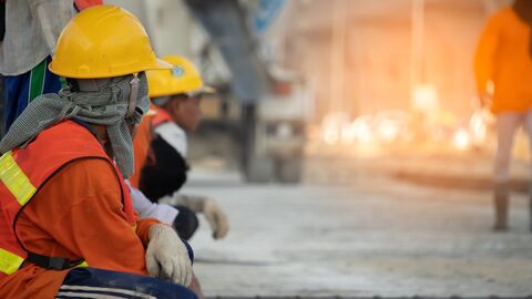 Zwei an einer Straße kniende Personen mit Bauhelm 