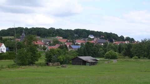 Holzstall Vordergrund, dahinter ein Dorf