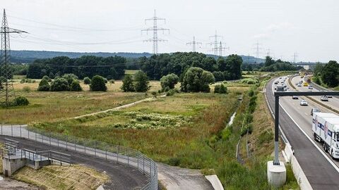 Strommasten in Landschaft, am rechten Bildrand Autobahn mit Fahrzeugen