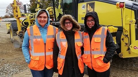 Die drei Auszubildenden mit Warnwesten vor einem Radlader