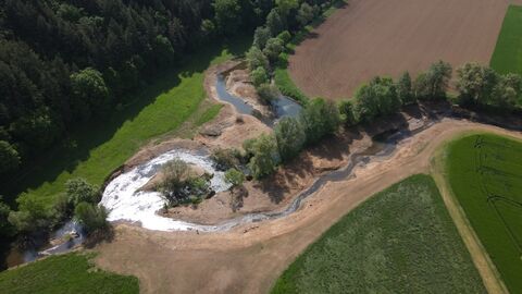 Luftbild eines Gewässers zwischen Wiesen