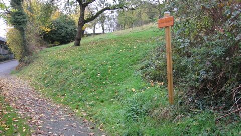 Biebertal-Vetzberg Belaubter Weg unterhalb eines Hanges, rechts ein Holzschild, im Hintergrund Bäume