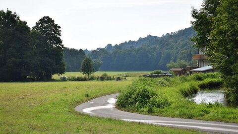 Weg mit Rechtskurve, daneben ein Bach, im Hintergrund Wald