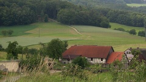 Blick auf ein Fachwerkhaus, dahinter Felder und Wald