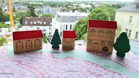 Immobilienwertermittlung 3 Häuser und 2 Bäume aus Bauklötzchen auf einem Stadtplan