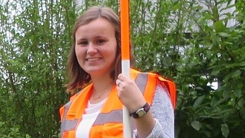 Auszubildende in orangefarbener Warnweste mit Fluchtstab