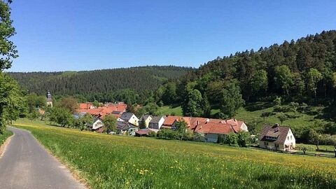 befestigter Weg führt links oberhalb von Häusern durch grüne Landschaft