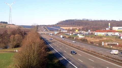 Autobahn, rechts davon Gewerbegebiet, im Hintergrund links ein Windrad