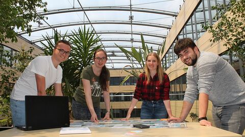 4 junge Menschen über einen Tisch gebeugt