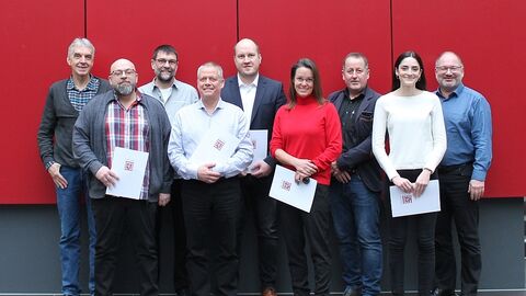 Neun Personen vor einer roten Wand