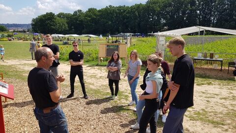 Foto im Freien von der Landesgartenschau 2023. Mehrere junge Menschen stehen im Halbkreis um einen Mann, der etwas erklärt.