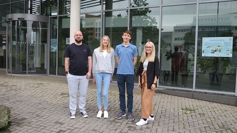 4 Menschen nebeneinander vor einer Glasfassade