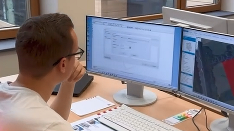 Junger Mensch schaut am Schreibtisch auf einen Monitor