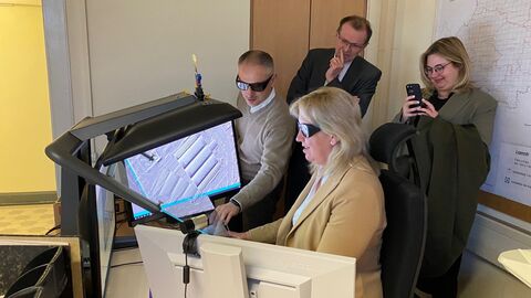 4 Personen in einem Büro, 2 Personen sitzen mit 3D-Brillen vor einem PC, 2 Personen stehen dahinter