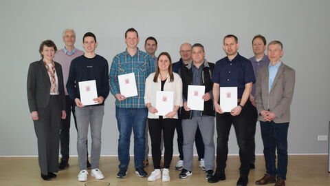 Gruppenbild von Personen vom AfB Fulda, die befördert wurden, ihre Urkunden zeigen und lächeln