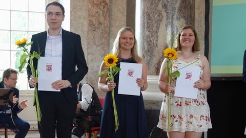 Freisprechungsfeier 2024 3 Personen mit Zeugnissen vor einer Präsentationswand