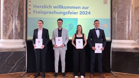 Freisprechungsfeier 2024 4 Personen mit Zeugnissen vor einer Präsentationswand