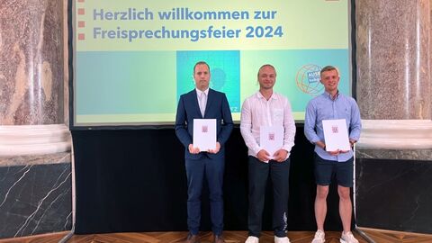 Freisprechungsfeier 2024 3 Personen mit Zeugnissen vor einer Präsentationswand