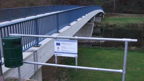 Schräg aufgenommene Brücke mit Abfalleimer und Schild