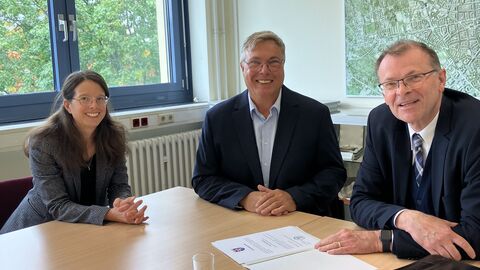 Drei Personen sitzen an einem Schreibtisch.