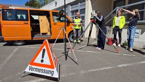 4 Personen vor Garagentor, im Hintergrund ein orangefarbener VW-Bus, im Vordergrund ein Gefahrenhinweis "Vermessung"